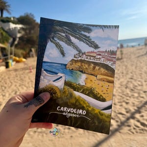Pode incluir: Um postal com uma ilustração costeira, com o texto "CARVOEIRO algarve". A obra de arte retrata uma praia, falésias, edifícios e palmeiras sob um céu azul. A assinatura do artista "JULECAS ART" é visível.