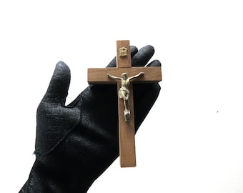 May include: Wooden crucifix with a silver-toned Jesus figure. The cross is held against a white background. The cross has a small metal plaque at the top. The figure of Jesus is detailed.