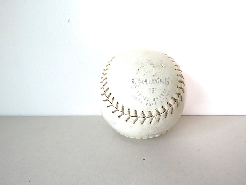 Puede incluir: Una pelota de softball de cuero blanco con costuras marrones y el logotipo de Spalding y "751" impreso en ella.