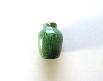 May include: A small, green ceramic vase with a rounded body and a narrow neck. The vase has a textured surface and a slightly chipped rim. The color is a deep, mottled green.