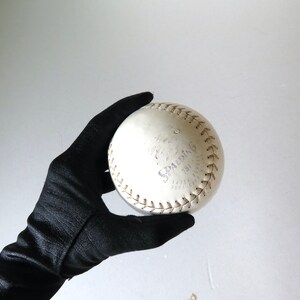 Puede incluir: Una pelota de softball blanca con la palabra "SPALDING" escrita en negro. La pelota se sostiene en un guante negro.