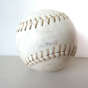 Puede incluir: Una pelota de softbol de cuero blanco con costuras marrones. La pelota tiene el texto "Official Softball" y "12" impreso en ella.