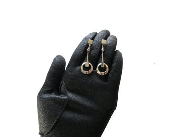 May include: Silver-toned dangle earrings. Each earring features a small square stud, a slender vertical bar, and a circular hoop. The earrings are displayed against a black background.