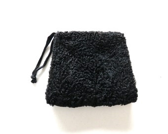 May include: A black, textured pouch with a drawstring closure. The pouch has a square shape and a soft, curly texture. The drawstring is a thin, black cord. The background is plain white.