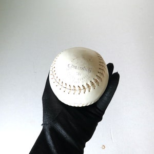 Puede incluir: Una pelota de softball blanca con costuras marrones y el logotipo de Spalding y "751" impreso en ella.