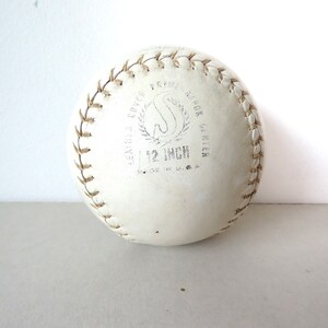 Puede incluir: Una pelota de softball de cuero blanco de 30,5 cm con costuras marrones y el texto "LEATHER COVER  PRO  A.B.O.K.  GRIPPER  12 INCH  MADE IN U.S.A."