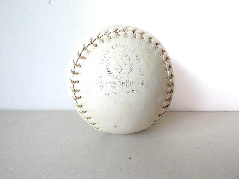 Puede incluir: Una pelota de softball de cuero blanco de 30,5 cm con costuras marrones y el texto "LEATHER COVER  PRO  A.B.O.K.  GRIPPER  12 INCH  MADE IN U.S.A."