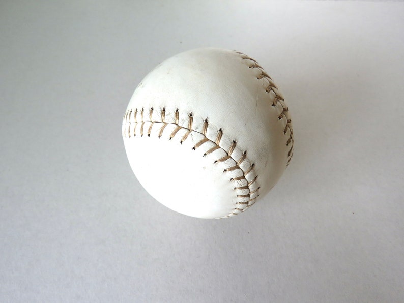 Puede incluir: Una pelota de softbol de cuero blanco con costuras marrones.