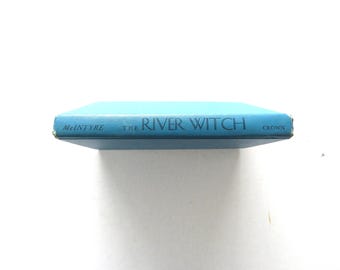 May include: A hardcover book titled "The River Witch" by McIntyre, with a light blue cover and dark blue lettering. The word "Crown" is also visible. The book is set against a white background.