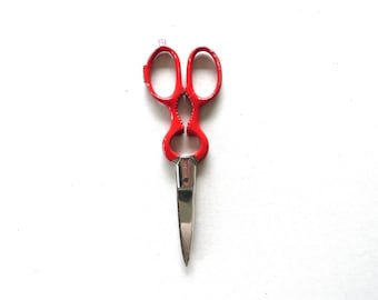 May include: Red kitchen shears with a stainless steel blade. The shears have a bottle opener and a nutcracker function. The handles are bright red and have finger holes for easy gripping. The shears are designed for various kitchen tasks.