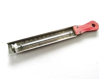 May include: Vintage Taylor Deep Frying Guide thermometer with a red wooden handle. The thermometer has a metal casing with temperature markings and a glass tube. The text "Taylor DEEP FRYING GUIDE" is printed on the metal casing.