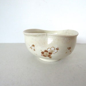 May include: A small, white ceramic bowl with a slightly wavy rim. The bowl has a brown and white floral pattern.