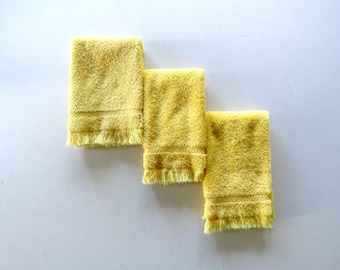 May include: Three yellow hand towels with fringed edges and decorative stitching. The towels are arranged in a staggered row, showcasing their soft, absorbent texture. A simple, yet practical addition to any bathroom.