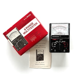 May include: A red and white Micronta 8-Range Multitester box, a black multitester, and an owner's manual. The multitester has a mirrored scale and rotary range selector. The box reads "2,000 ohms/volt".