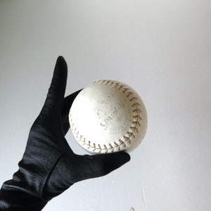 Puede incluir: Una pelota de softball blanca con costuras marrones y la palabra "SPALDING" impresa en ella.