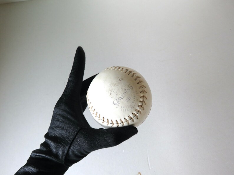 Puede incluir: Una pelota de softball blanca con costuras marrones y la palabra "SPALDING" impresa en ella.
