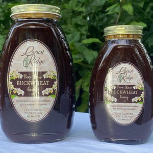 May include: Two glass jars of Locust Ridge Apiaries Pure Raw Buckwheat Honey. The jars are labeled with the company name and product information. The honey is a dark brown color.