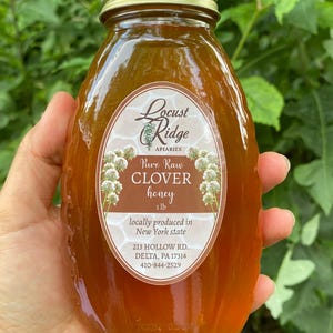May include: A glass jar of raw clover honey from Locust Ridge Apiaries in New York state. The jar is labeled with the company name, product name, weight, and contact information. The honey is a light amber color.