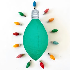 May include: A green lightbulb shaped pillow surrounded by 12 colorful lightbulbs. The lightbulbs are in various colors, including red, yellow, blue, and green.