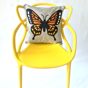 May include: A yellow chair with a butterfly pillow. The pillow is gray with a black and orange butterfly design.