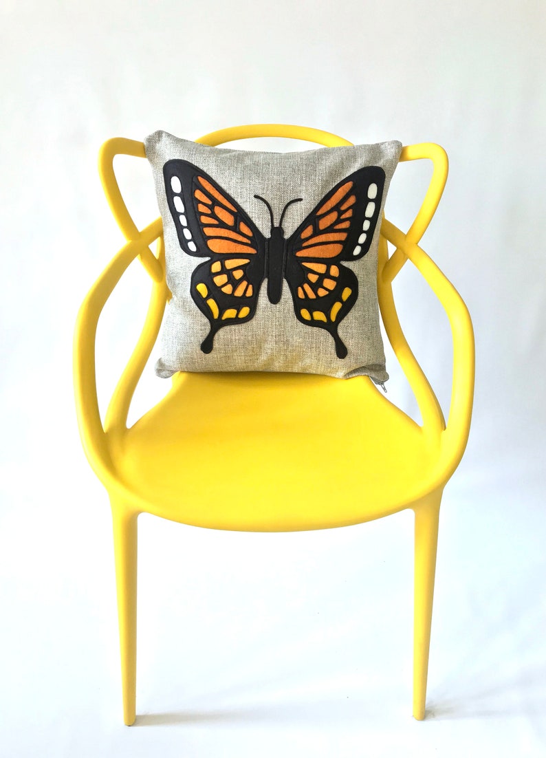 May include: A yellow chair with a butterfly pillow. The pillow is gray with a black and orange butterfly design.