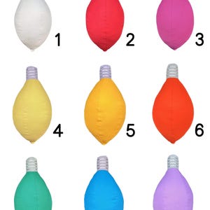 May include: Nine light bulb shaped pillows in different colors: white, red, pink, yellow, orange, green, blue, and purple. The pillows are arranged in three rows of three.