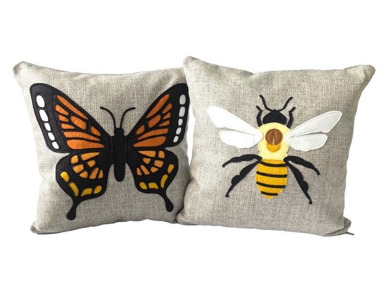 May include: Two decorative throw pillows with embroidered designs. One pillow features a black and orange butterfly with white accents. The other pillow features a yellow and black bee with white wings.