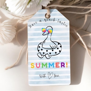 Puede incluir: Una etiqueta de regalo con un pato de dibujos animados con gafas de sol y una boya. La etiqueta tiene el texto "Have a quack-tastic SUMMER! With love." El fondo es azul claro con rayas blancas, atada con hilo.