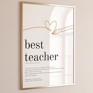 May include: A framed print with a gold-colored frame. The print features the words "best teacher" in a black font, with a definition below. A gold-colored line drawing of a heart and paintbrush is at the top.
