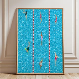 May include: A framed vertical art print depicting a bright blue swimming pool with white water ripples. Six swimmers in colorful swimsuits are positioned in lanes separated by red and white striped lane markers, captured in various swimming poses.