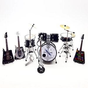 Op de afbeelding: Miniatuur rockband set met zwarte en zilveren gitaren, een zwarte drumstel en een microfoon. De drumstel heeft een witte basdrum met een cirkelvormig ontwerp. De set staat op een witte achtergrond.