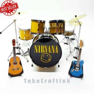 May include: A miniature drum kit with a black bass drum displaying "NIRVANA" in yellow, and a smiley face. It includes yellow and brown drums, cymbals, and two guitars. The set is set against a white backdrop.