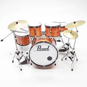 May include: A miniature drum set with a white bass drum that says "Pearl" in black lettering. The set includes a snare drum, two toms, and a cymbal. The drums are brown with a wood grain finish.