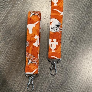 May include: Two orange and white fabric keychains with silver key rings. The keychains feature a football helmet, a longhorn steer, and the text "Texas".