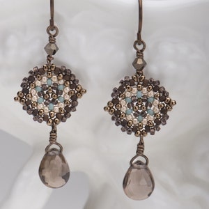 May include: A pair of dangle earrings with a geometric design made of brown, white, and blue beads. The earrings have a teardrop-shaped brown gemstone hanging from the bottom.