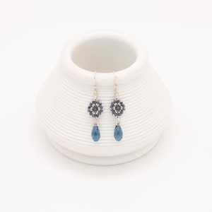 May include: A pair of silver dangle earrings with a blue crystal teardrop and a beaded flower design.