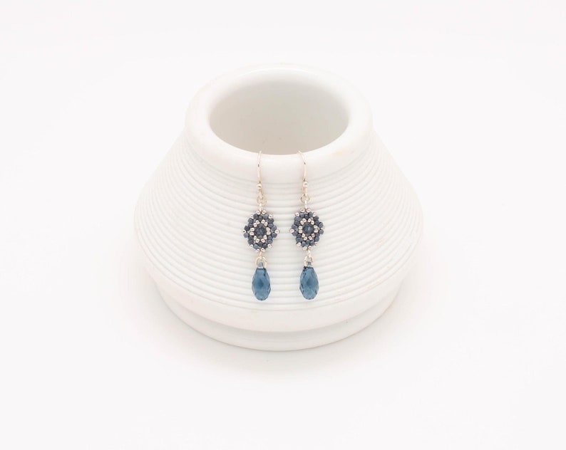 May include: A pair of silver dangle earrings with a blue crystal teardrop and a beaded flower design.