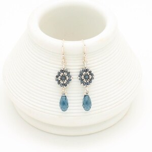 May include: A pair of silver dangle earrings with a blue crystal teardrop and a beaded flower design.