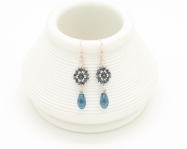 May include: A pair of silver dangle earrings with a blue crystal teardrop and a beaded flower design.