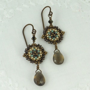 May include: A pair of dangle earrings with a brown, beige, and turquoise beaded design. Each earring features a teardrop-shaped brown gemstone.