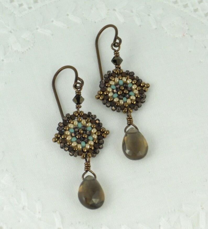 May include: A pair of dangle earrings with a brown, beige, and turquoise beaded design. Each earring features a teardrop-shaped brown gemstone.
