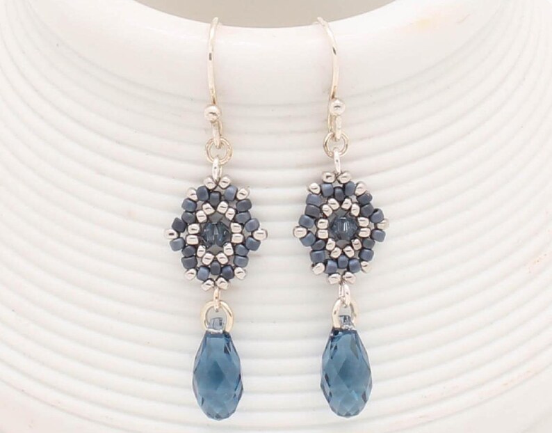May include: A pair of silver dangle earrings with a blue crystal teardrop and a hexagonal bead cluster. The bead cluster is made of silver and blue beads.