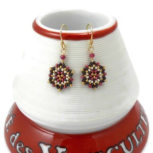 May include: A pair of gold dangle earrings with a brown, white, and red beaded snowflake design.