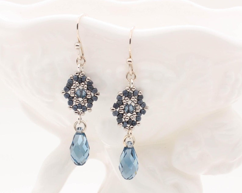 May include: Silver dangle earrings with a geometric bead design in shades of gray and a teardrop-shaped crystal pendant.