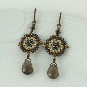 May include: A pair of dangle earrings with a geometric design made of brown, white, and turquoise beads. The earrings have a teardrop-shaped brown gemstone hanging from the bottom.
