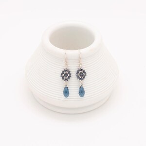May include: A pair of silver dangle earrings with a blue crystal teardrop and a beaded flower design.