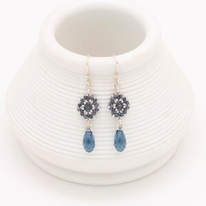May include: A pair of silver dangle earrings with a blue crystal teardrop and a geometric bead cluster.