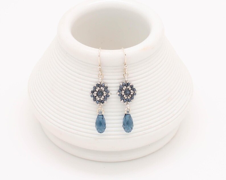 May include: A pair of silver dangle earrings with a blue crystal teardrop and a geometric bead cluster.