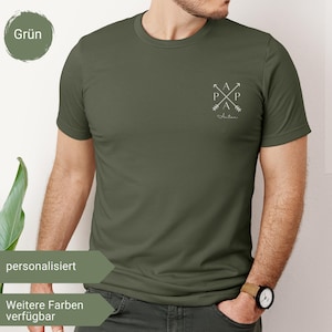 Pode incluir: T-shirt verde-oliva com gola redonda. A camisa apresenta um pequeno gráfico branco no peito com setas e as letras "A" e "P". A palavra "Anton" está escrita abaixo do gráfico. A camisa está sendo usada por uma pessoa.