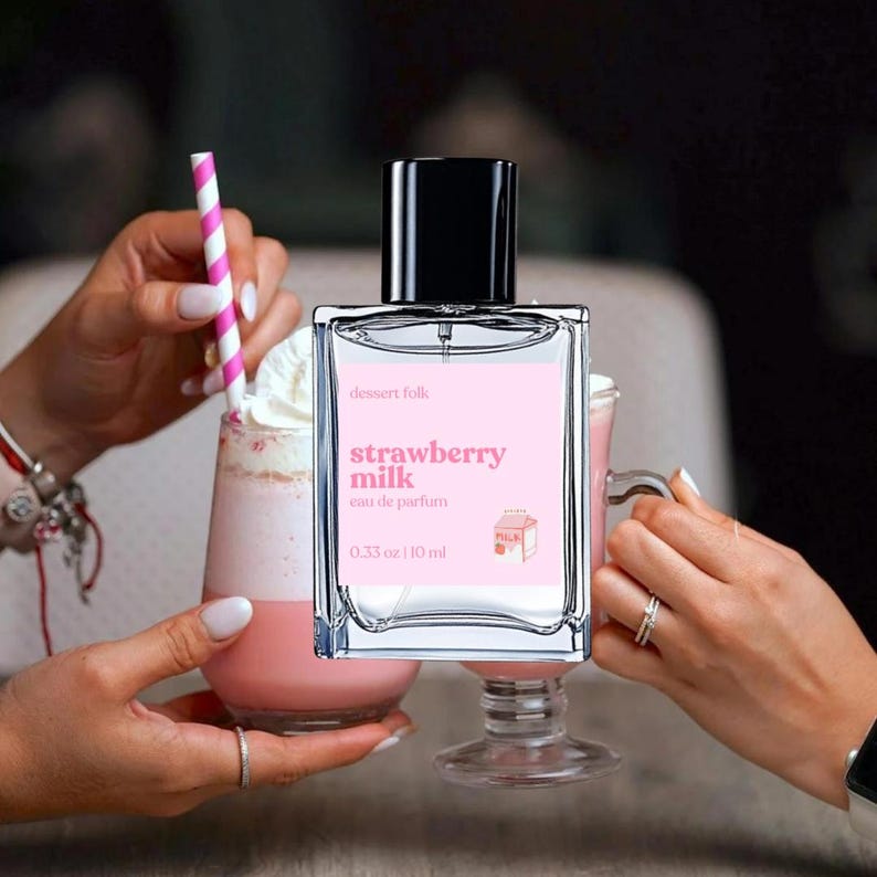 May include: Strawberry Milk Eau de Parfum by Dessert Folk.  A clear glass bottle with a black cap displays the product name and description against a pink background. The bottle is 0.33 oz / 10 ml. The fragrance is presented alongside two strawberry milk drinks.